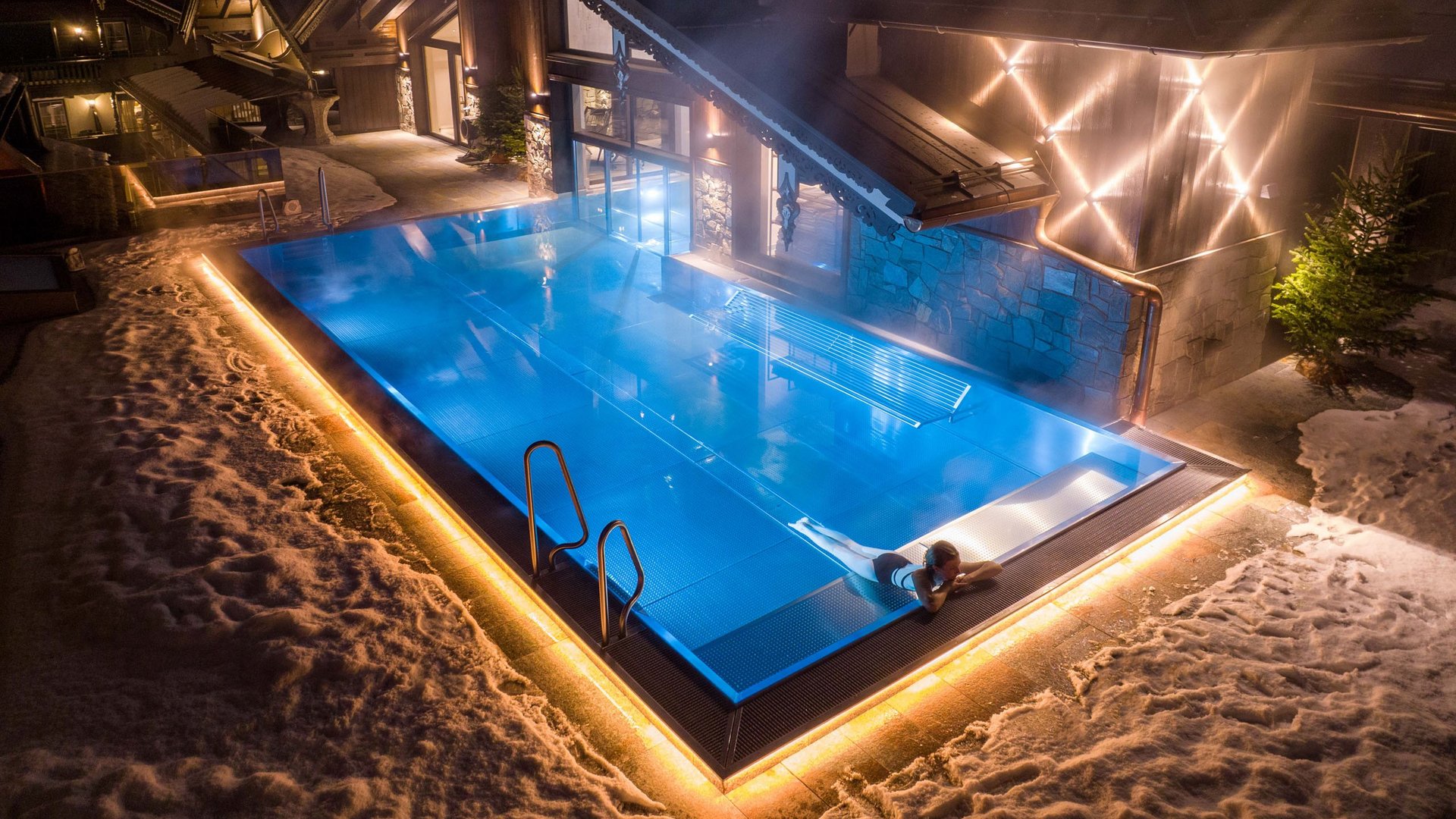 Beheizter Außenpool bei Nacht an einem Haus im Schnee mit Person im Wasser